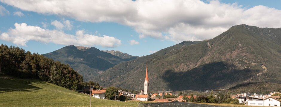 Dorf mit Kirchturm im Tal von Brixen Südtirol, umgeben von Bergen und Feldern