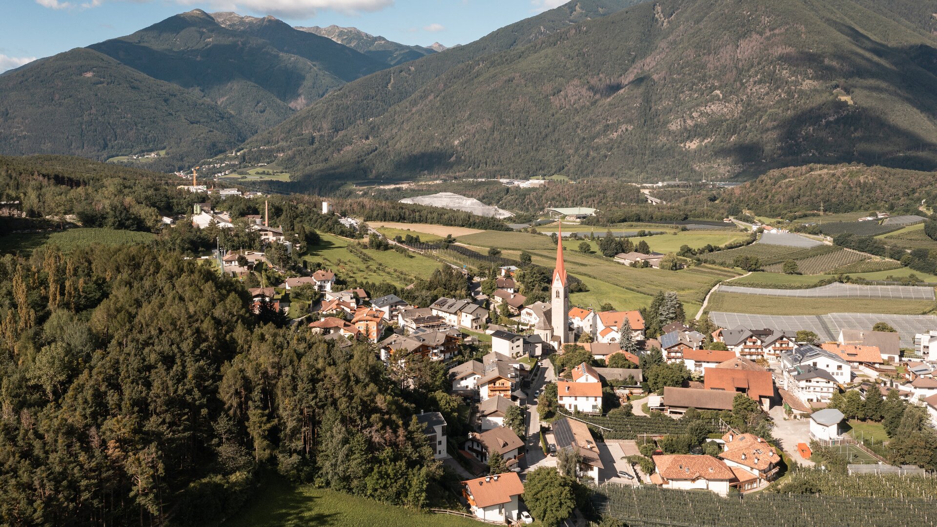 Village with a church spire in a green valley below the mountains.