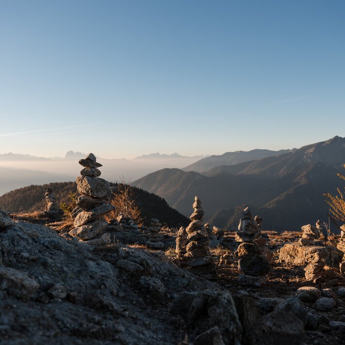 Stone cairns on a rocky mountain ridge at sunrise with distant peaks and clear sky