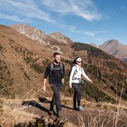 Two hikers on a mountain trail above a wooded valley in Brixen Südtirol.