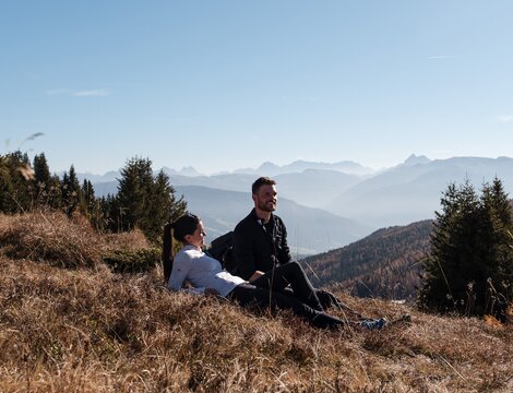Two hikers resting on a grassy slope with mountain views in Brixen Südtirol.