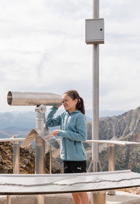 Donna osserva con un cannocchiale da un belvedere di montagna in Brixen Südtirol