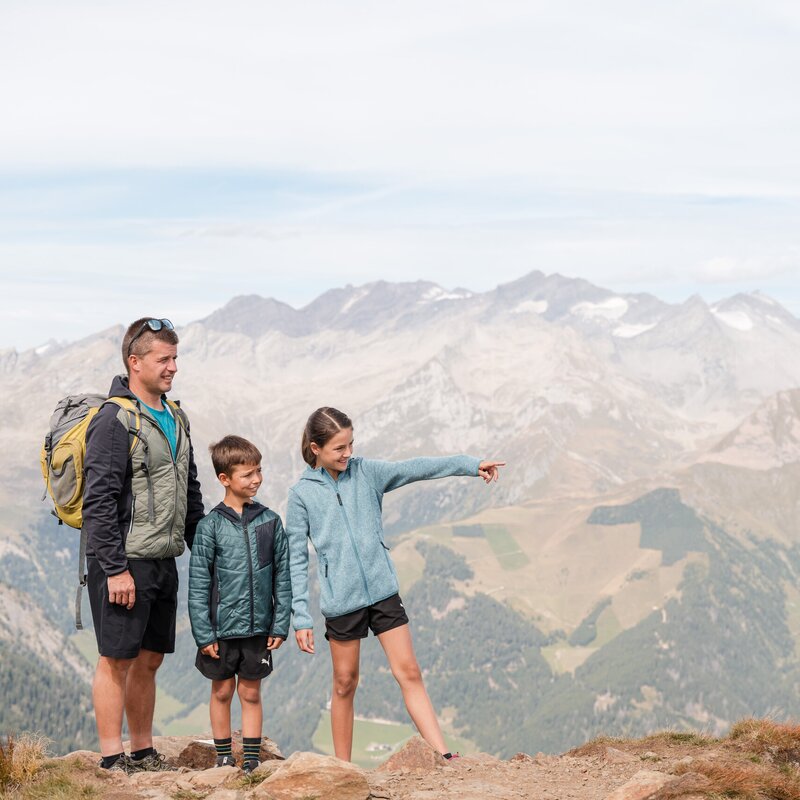 Familie beim Wandern auf einem Berggrat mit weitem Blick über die Alpen und Täler.