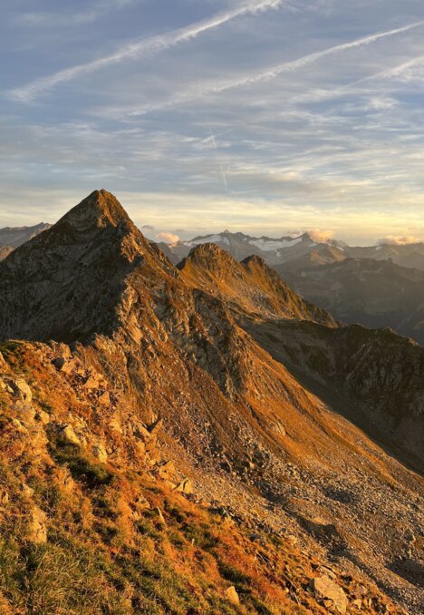 Licht auf einem felsigen Berggrat mit Gipfeln im warmen Morgenhimmel