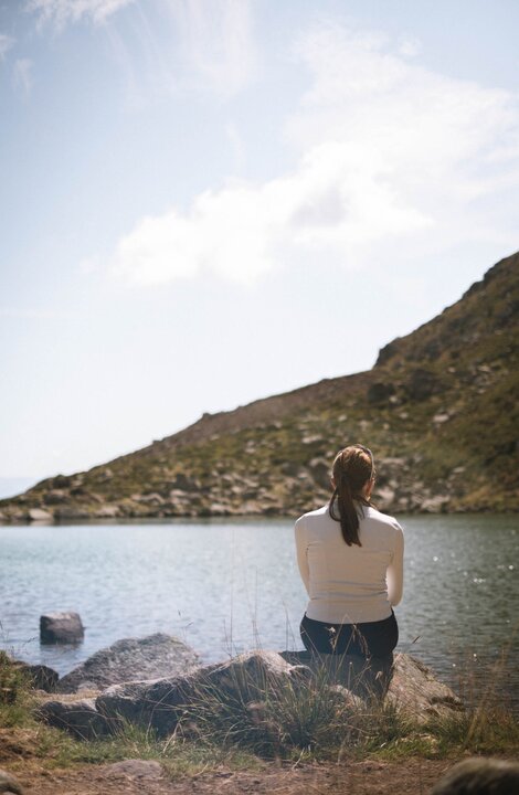 Woman sitting on rocks by a mountain lake on a clear day