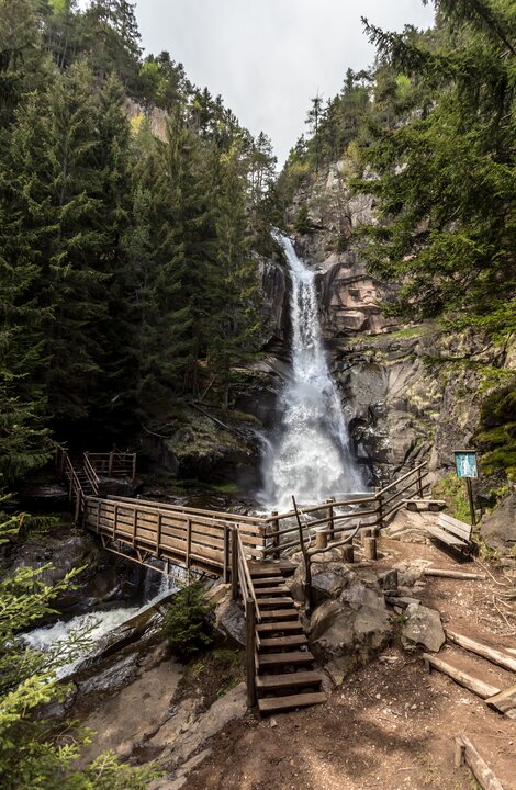 Wooden walkway leading to a waterfall in a forest canyon.