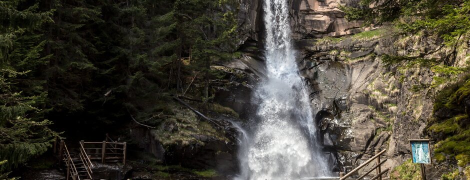 Passerella in legno con scale che porta a una cascata in una gola boscosa.