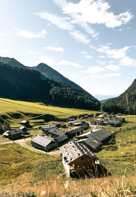 Sonniges Alpental mit kleinem Bergdorf, grünen Wiesen und bewaldeten Hängen in Brixen Südtirol.