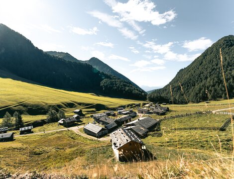 Valle alpina soleggiata con piccolo villaggio di montagna, prati verdi e versanti boscosi a Brixen Südtirol.