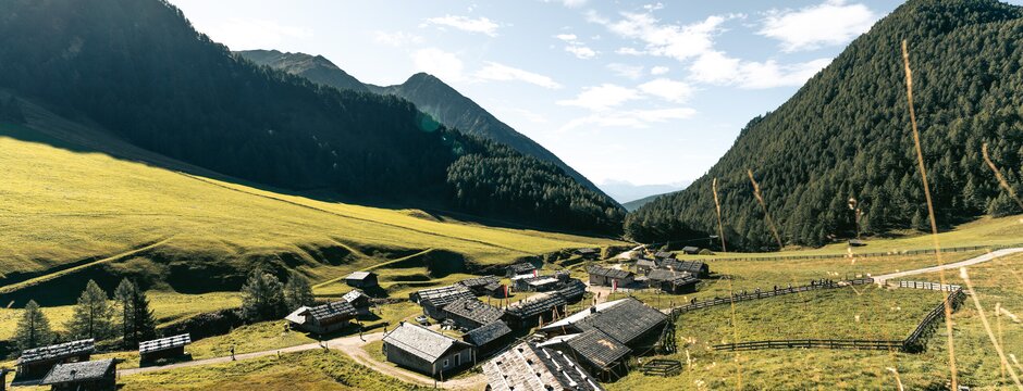 Sonniges Alpental mit kleinem Bergdorf, grünen Wiesen und bewaldeten Hängen in Brixen Südtirol.