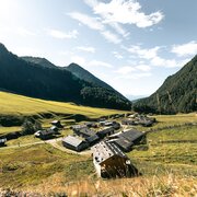 Valle alpina soleggiata con piccolo villaggio di montagna, prati verdi e versanti boscosi a Brixen Südtirol.