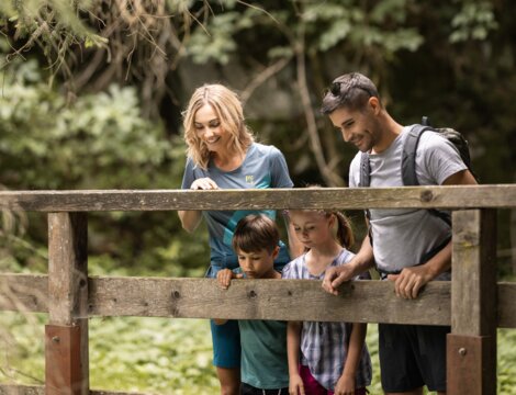 Familie mit zwei Kindern an einem Holzgeländer im grünen Wald