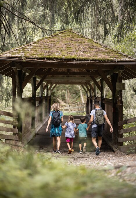 Familie mit Kindern geht über eine überdachte Holzbrücke in Brixen Südtirol.