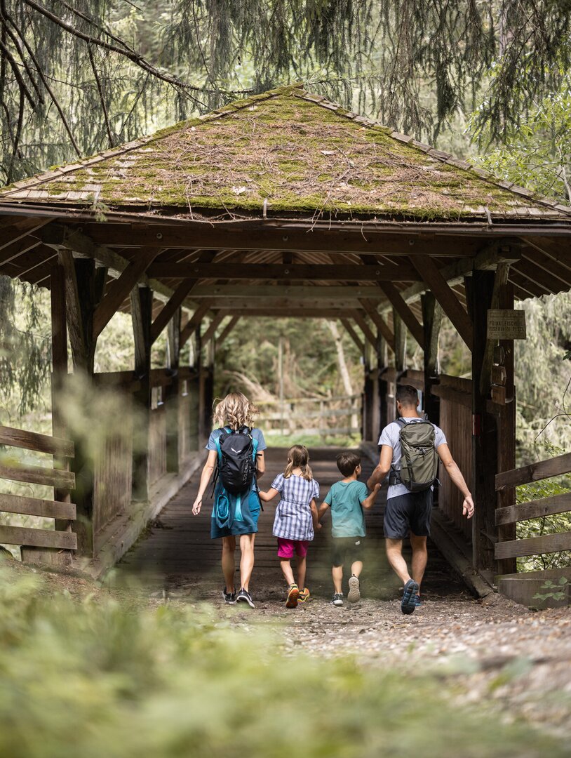 Famiglia con bambini che attraversa un ponte coperto in legno a Brixen Südtirol.
