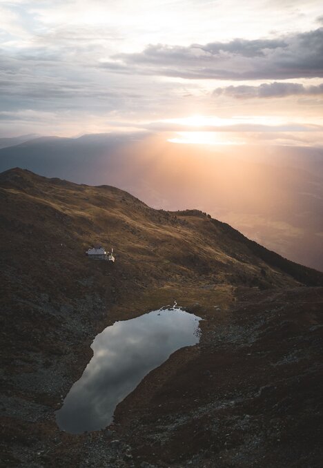 Sonnenaufgang über Bergsee und Grat in einer kargen alpinen Landschaft.