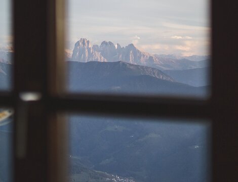 Berggipfel durch ein Fenster mit Tal darunter und weichem Abendlicht.