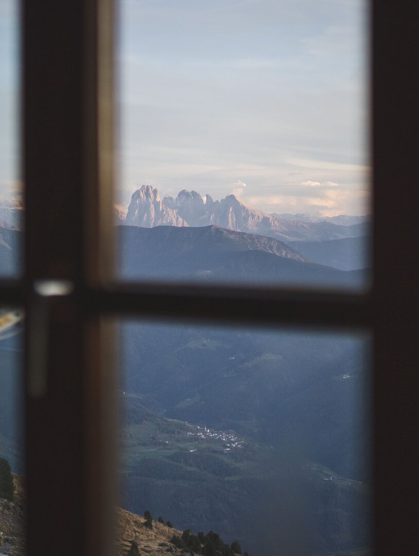 Berggipfel durch ein Fenster mit Tal darunter und weichem Abendlicht.