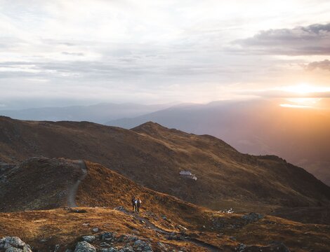 Escursionisti su un crinale di montagna al tramonto con vista sulla valle e luce calda sulle cime.