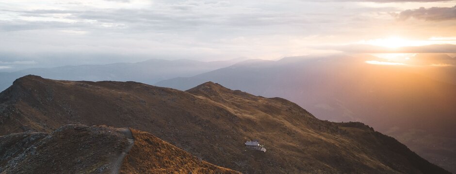 Hikers on a mountain ridge at sunset with valley views and warm light over the peaks.