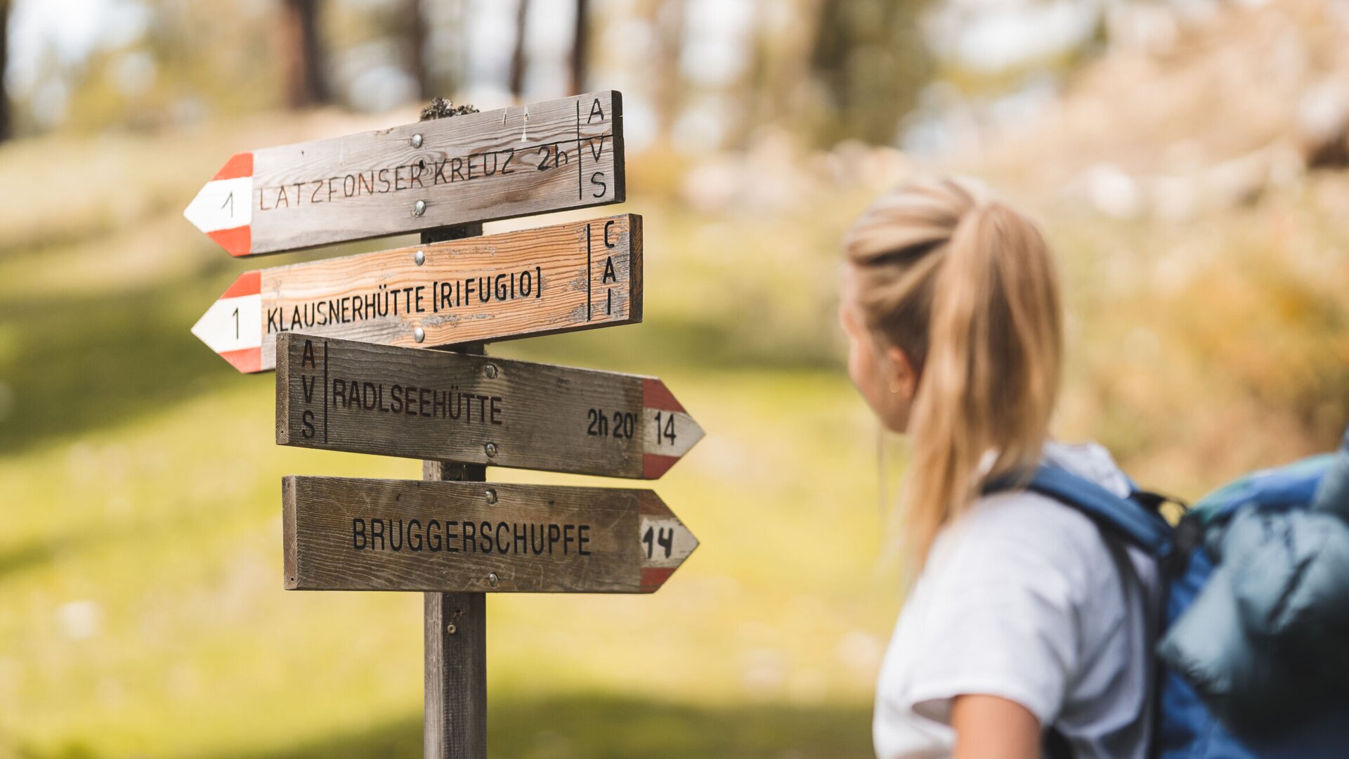 Wanderin neben Holzwegweisern im Wald bei Brixen Südtirol