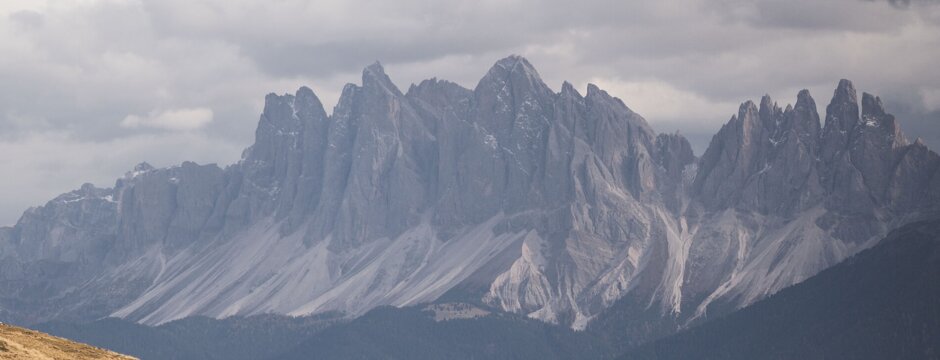 Pendio alpino erboso con cime dolomitiche frastagliate sotto un cielo nuvoloso