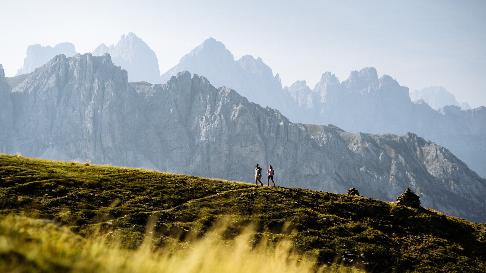 Wanderer auf einem grasigen Grat mit den Dolomiten im Hintergrund.
