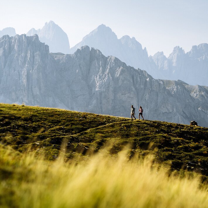 Hikers on a grassy ridge with the Dolomite mountains in the background.