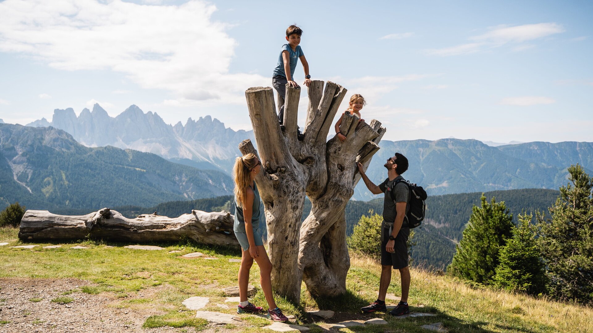 Family with two children at a large tree stump overlooking the Brixen Südtirol mountains on a sunny day.
