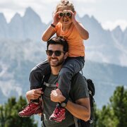 Padre con un bambino sulle spalle davanti alle montagne sullo sfondo.