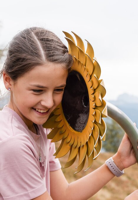 Ragazza sorridente con una scultura a forma di girasole su un prato di montagna.