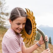 Lächelndes Mädchen hält eine Sonnenblumen-Skulptur auf einer Bergwiese.