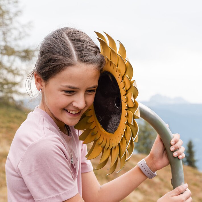 Lächelndes Mädchen hält eine Sonnenblumen-Skulptur auf einer Bergwiese.