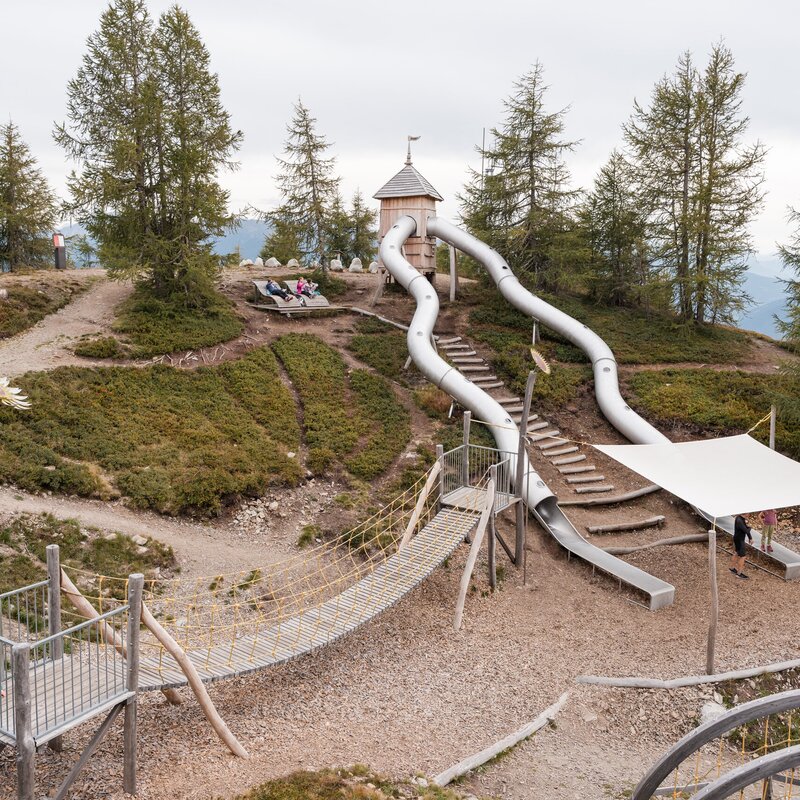 Bergspielplatz mit Rutschen, Hängebrücke und Wald in Südtirol.