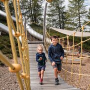 Due bambini attraversano un ponte sospeso in un parco avventura nel bosco.