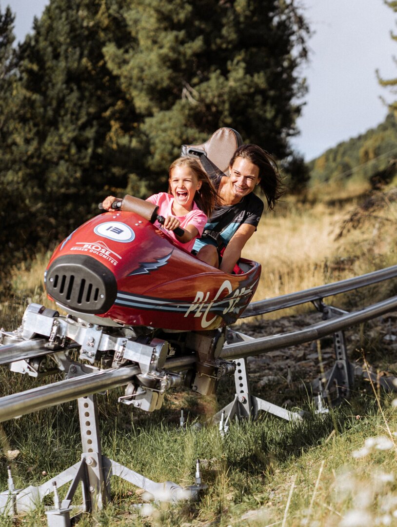 Donna e bambino su una slittovia rossa su un pendio erboso in montagna a Brixen Südtirol.