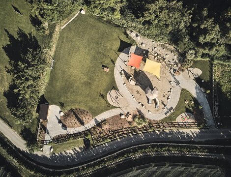 Vista aerea di un parco giochi con vele d’ombra, prato e alberi accanto alla strada.
