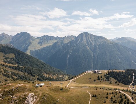 Panorama montano soleggiato con prati alpini, sentieri e cime rocciose.