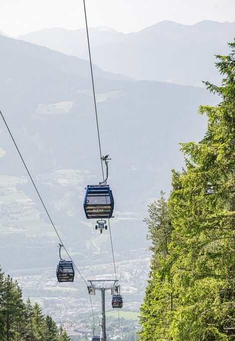 Cabinovie sopra una valle verde con le montagne sullo sfondo.