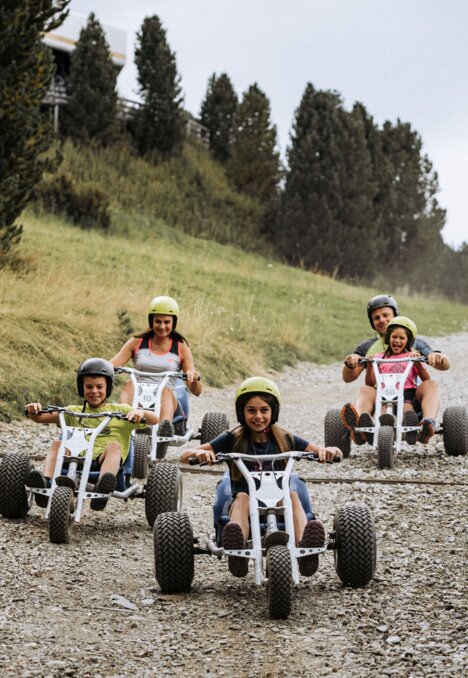Familie fährt mit Mountaincarts auf einem Schotterhang in Brixen Südtirol