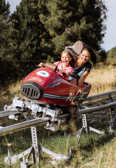Frau und Kind auf der Sommerrodelbahn im Gras bei Brixen Südtirol.