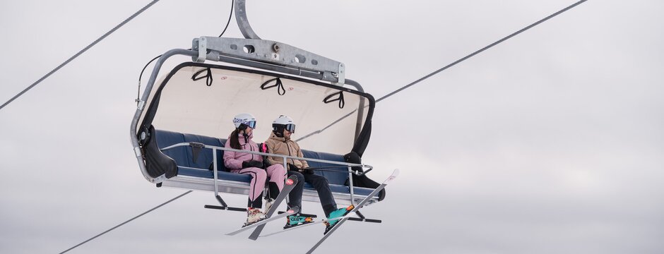Twee skiërs zitten op een stoeltjeslift boven een besneeuwde berghelling in Brixen Südtirol.