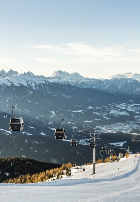 Skipiste met gondelliften boven een winterdal en besneeuwde bergtoppen. | © Hannes Niederkofler