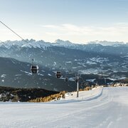 Pista da sci con funivie sopra una valle invernale e cime innevate.