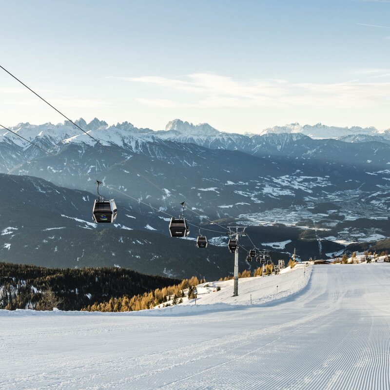 Pista da sci con funivie sopra una valle invernale e cime innevate.