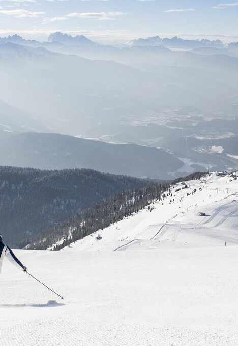 Sciatore in discesa su un pendio innevato con ampio panorama alpino a Brixen Südtirol.