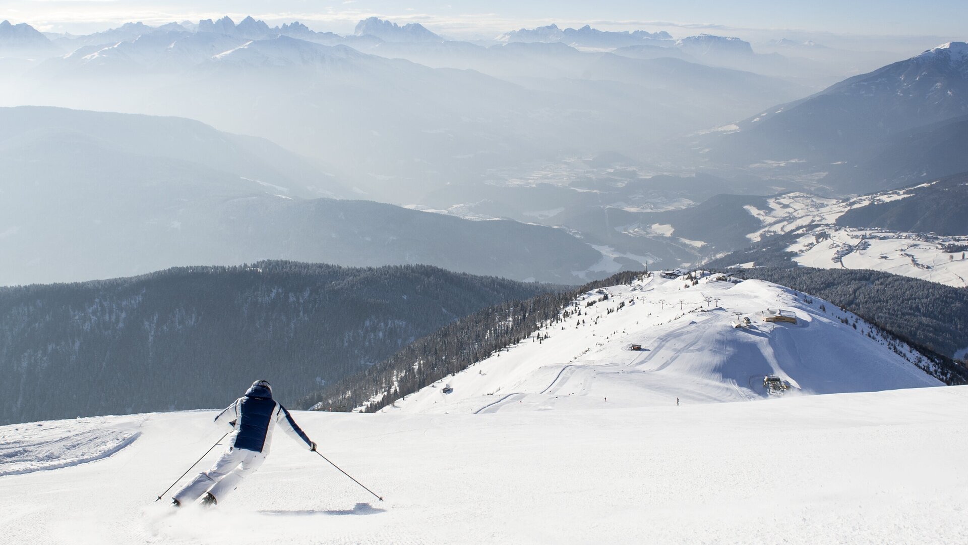 Skier descending a snowy mountain slope with wide alpine views in Brixen Südtirol.