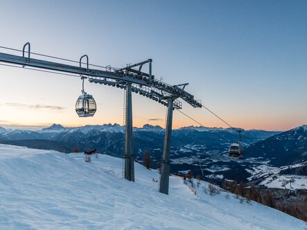Skilift über verschneiter Berglandschaft bei Sonnenuntergang, mit dem Tal darunter.