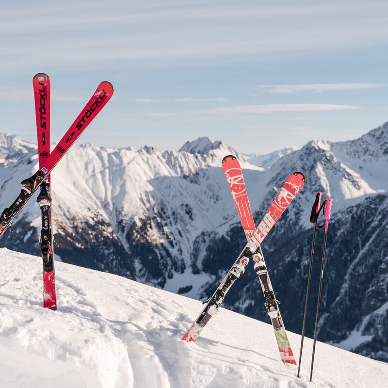 Sci rossi conficcati nella neve fresca, con cime alpine innevate sullo sfondo.