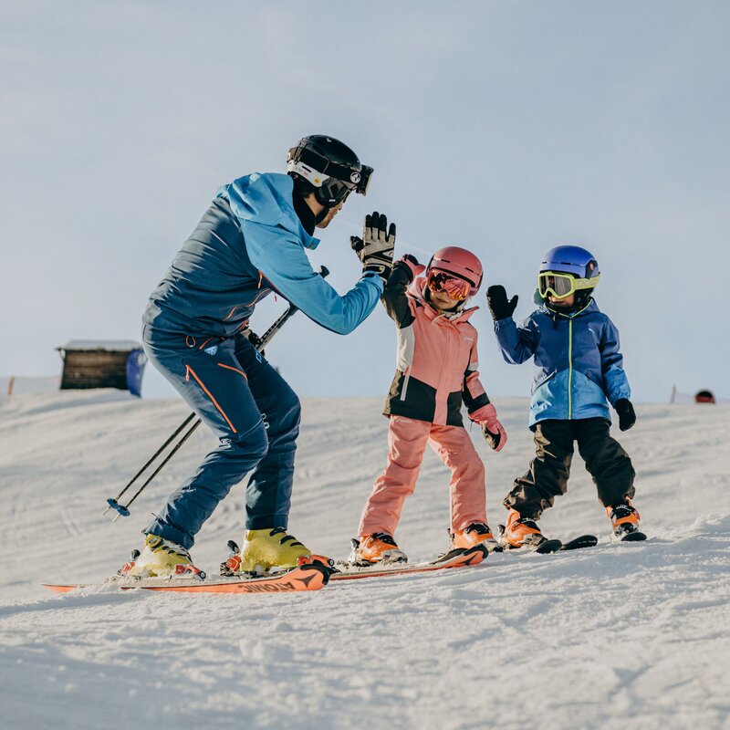 Ski instructor high-fives two children on a snowy slope in winter.
