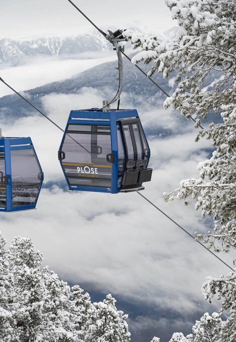 Cabine della funivia blu sopra alberi innevati e una valle di montagna nebbiosa in inverno